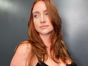 Woman with red hair and a black top standing in front of a gray background at THE LONDONER in Hermosa Beach.