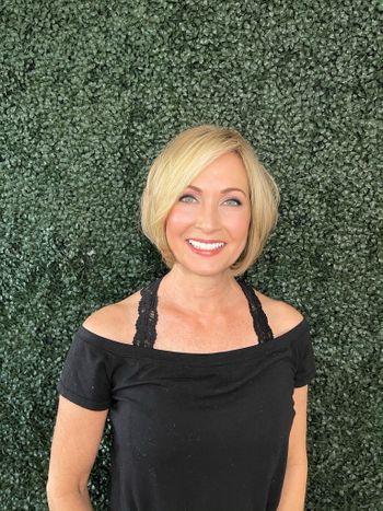 Woman with a black top and styled blonde hair standing in front of a luscious garden wall at THE LONDONER in Hermosa Beach.