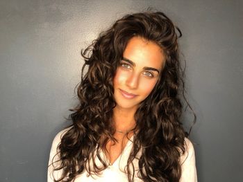 Woman with long, curly brown hair wearing a white top and standing in front of a gray background inside of THE LONDONER in Hermosa Beach.