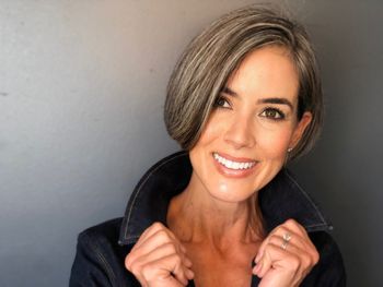 Woman wearing a black jacket standing in front of a gray background after a haircut appointment at THE LONDONER in Hermosa Beach.