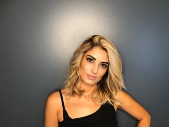 Blonde woman with a black top standing in front of a gray background after getting her hair styled at THE LONDONER in Hermosa Beach.
