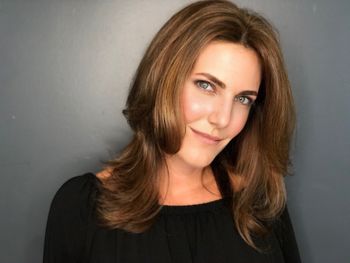 Woman with styled brown hair wearing a black top smiling after a hair styling appointment at THE LONDONER in Hermosa Beach.