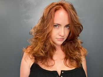 Woman with red hair wearing a black top standing in front of a gray background at THE LONDONER in Hermosa Beach.