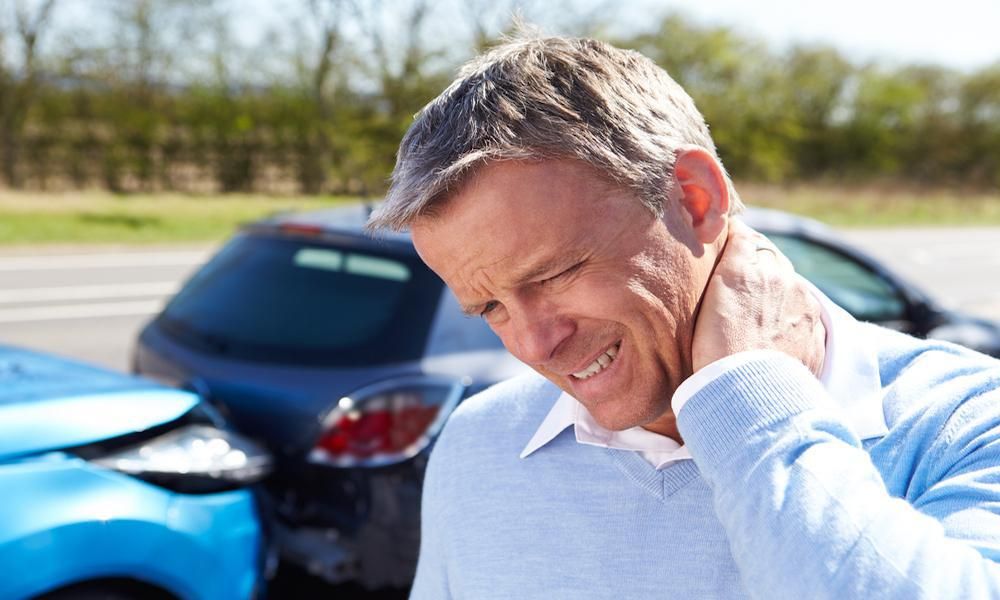 man holds his neck in front of a car wreck