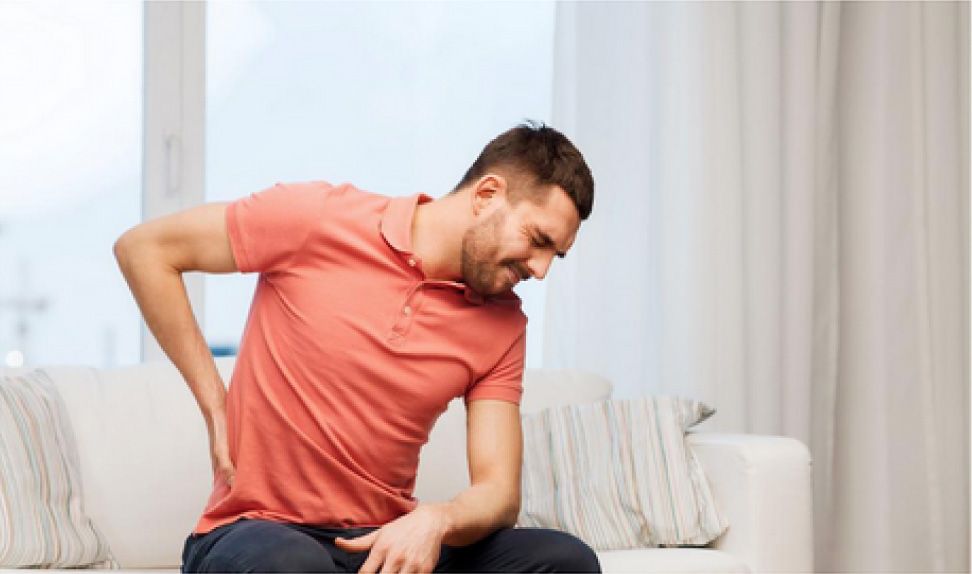 man holds his back and has a look of pain on his face