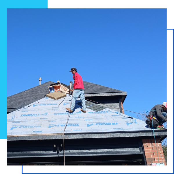Professional roofer securing shingles at the peak of a residential roof over protective blue synthetic underlayment.