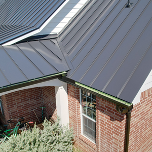 Detail shot of a dark matte metal roof installation on a brick home with integrated black gutter systems.