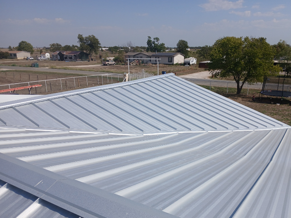 Wide-angle view of a completed silver PBR metal roof on a residential property in a rural Texas setting.