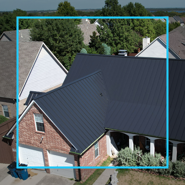 Aerial view of a residential home featuring a modern charcoal grey standing seam metal roof and classic red brick exterior.