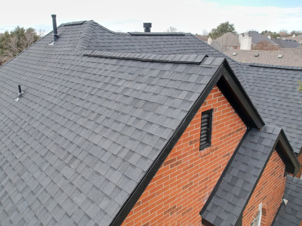 High-angle view of a residential charcoal asphalt shingle roof with integrated vents on a red brick house.