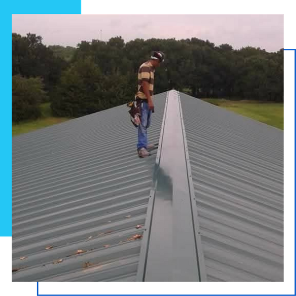 A professional roofer standing on the ridge of a dark green ribbed metal roof during a quality inspection.
