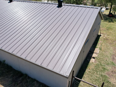Side view of a large metal shop or barn with a brown ribbed roof and light grey corrugated metal siding.