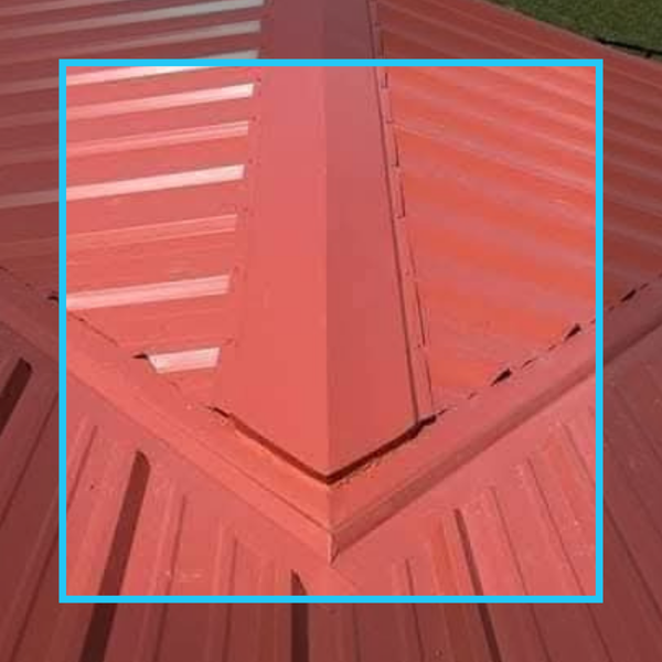 Detail shot of a vibrant red metal roof where the ridge cap meets a valley, showcasing precise metal flashing.