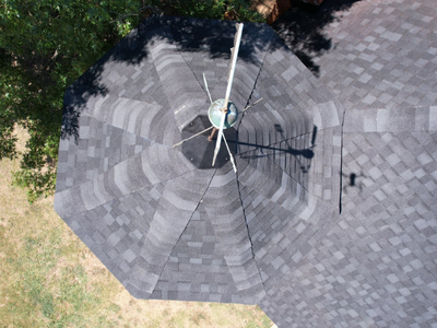 Top-down view of a circular roof turret finished with dark grey shingles and a decorative metal finial on top.