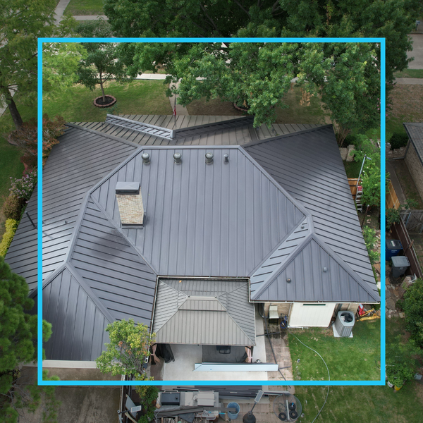 Top-down aerial view of a dark charcoal standing seam metal roof with precise flashing around a central brick chimney.