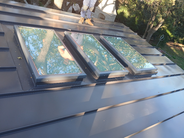 Three large glass skylights professionally integrated into a dark grey standing seam metal roof.