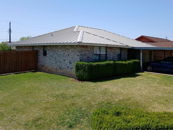 Side view of a grey brick residential home with a high-quality light grey metal roof installation.
