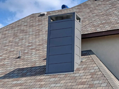 A custom-fabricated charcoal grey metal chimney shroud professionally installed on a shingle roof.