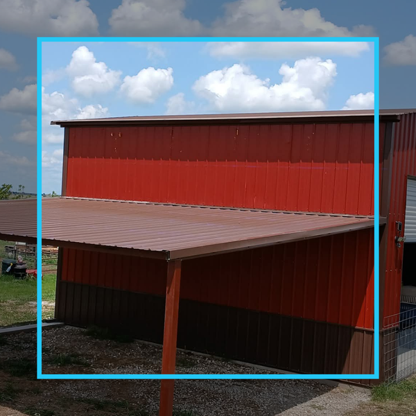 A red metal storage building or barn with a brown metal awning extension and matching dark brown base trim.