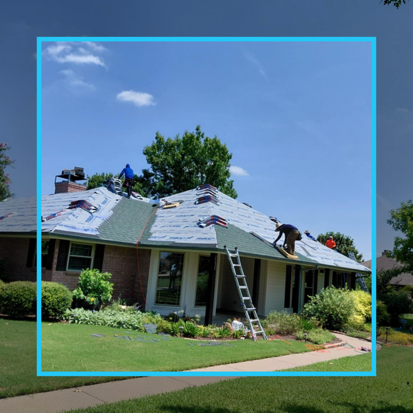 Roofing crew installing charcoal grey shingles over blue synthetic underlayment on a large residential roof.