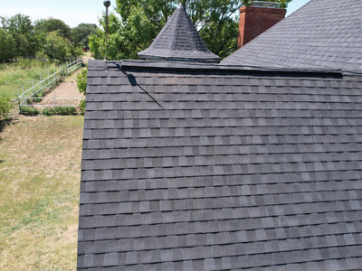 Close-up aerial view of a steep charcoal grey asphalt shingle roof installation with clean ridge lines.