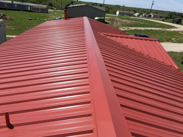 Perspective view of a long building featuring a vibrant red ribbed metal roof and matching ridge cap.