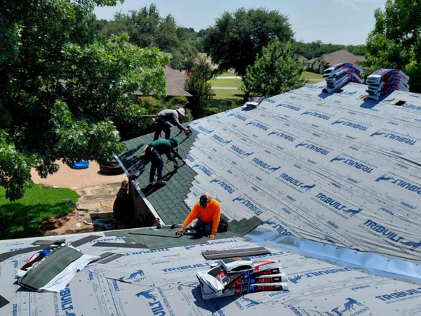  Roofing contractors precisely installing dark asphalt shingles over blue synthetic underlayment on a residential property.
