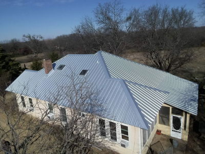 High-angle view of a residential home with a light grey metal roof featuring multiple skylights and a brick chimney.