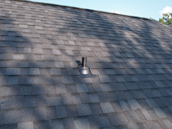 Close-up of a professionally installed black plumbing vent pipe and flashing on a charcoal grey shingle roof.
