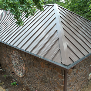 High-angle view of a bronze-toned metal roof installed on a rustic stone building surrounded by trees.