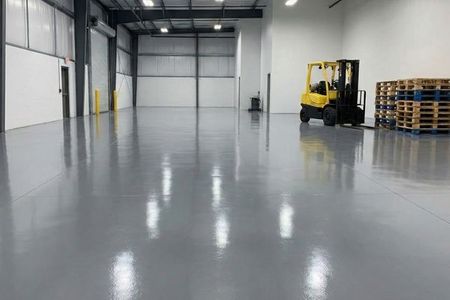 A large, clean commercial warehouse space with a seamless, high-gloss gray epoxy floor and a forklift in the background.