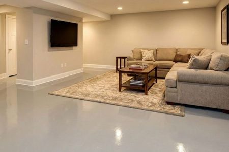 A finished basement family room featuring a light gray epoxy basement floor that reflects the overhead lights.