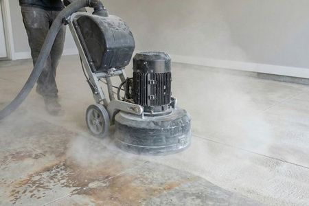 Concrete preparation process showing a diamond grinder removing old stains to create a clean surface for coating