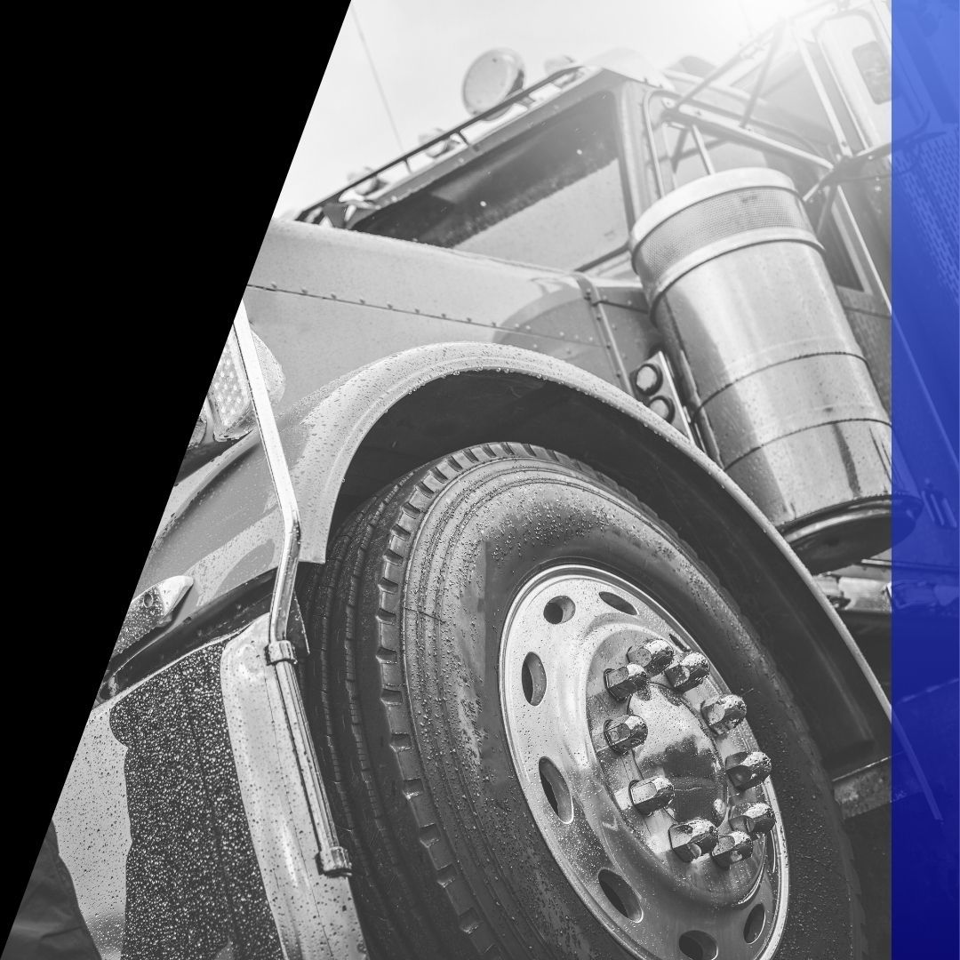 Low-angle shot of a large, wet semi-truck tire and polished fuel tank, emphasizing heavy duty vehicle service in any weather.