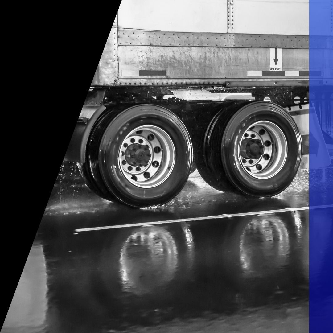 Close-up of the rear wheels of a semi-trailer reflecting in a puddle, emphasizing reliable semi-truck brake repair service.
