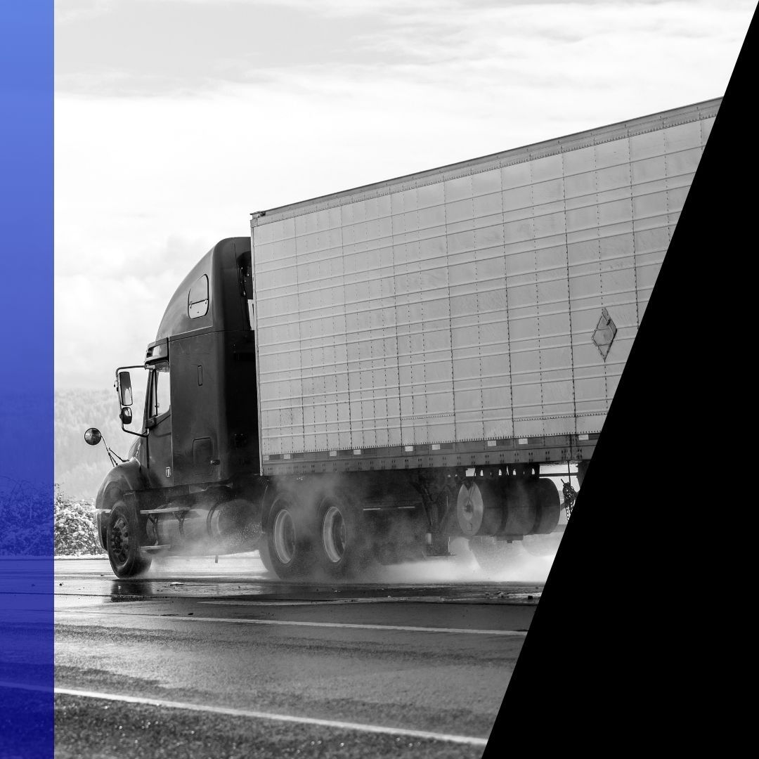 Black and white photo of a semi-truck with a white trailer driving on a wet road, showing the importance of heavy-duty semi-truck brakes.