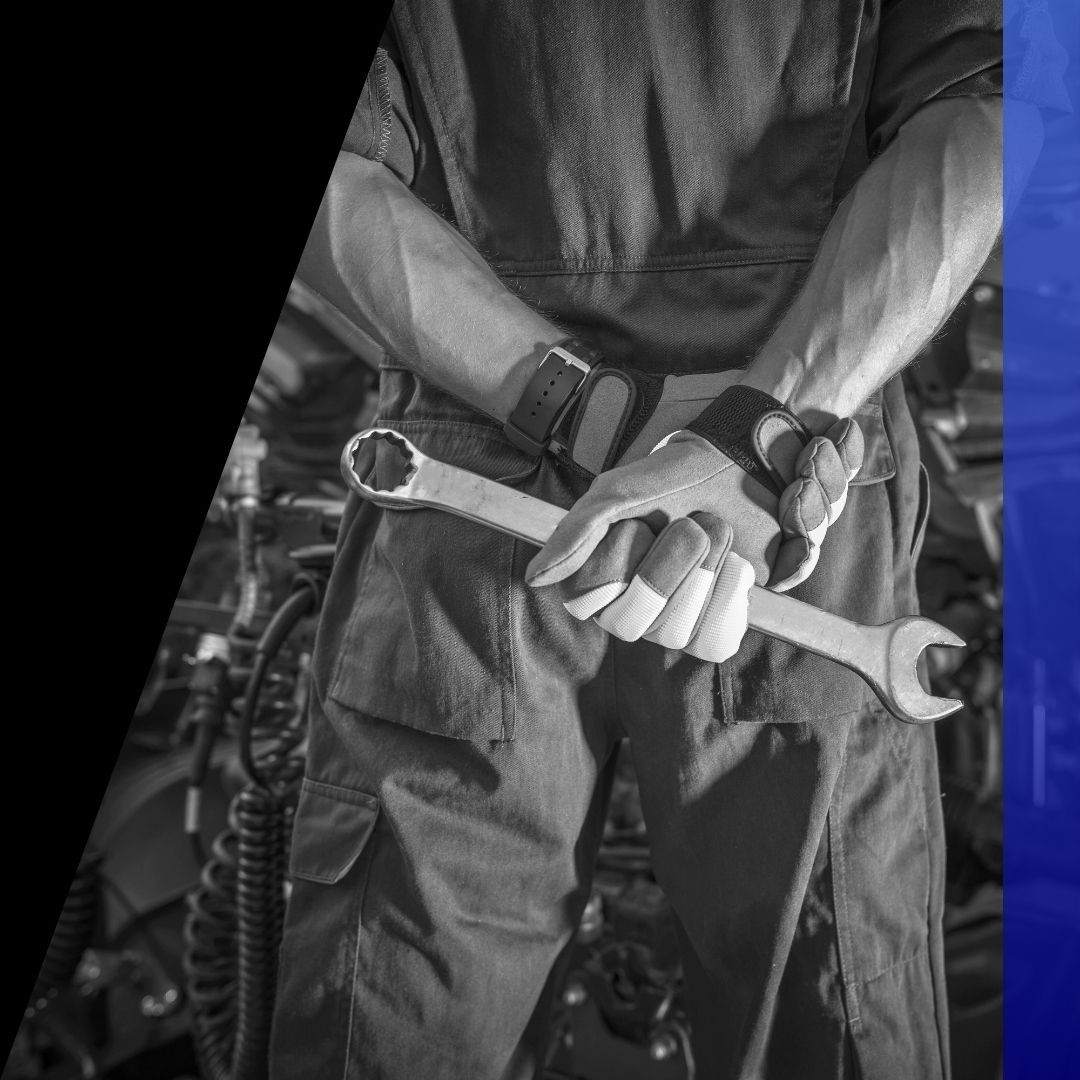 Close-up of a male mechanic's hands in gloves holding a large wrench behind his back, conveying expertise and readiness for repair.