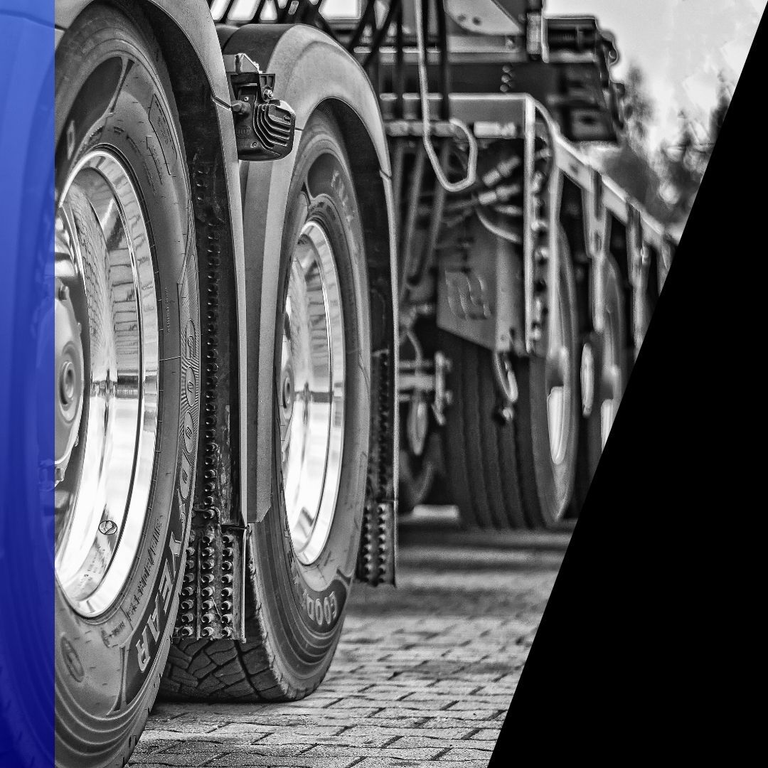 Close-up, black and white photo of multiple semi-truck tires and wheels parked on a brick surface, highlighting the large scale of commercial vehicle tires.