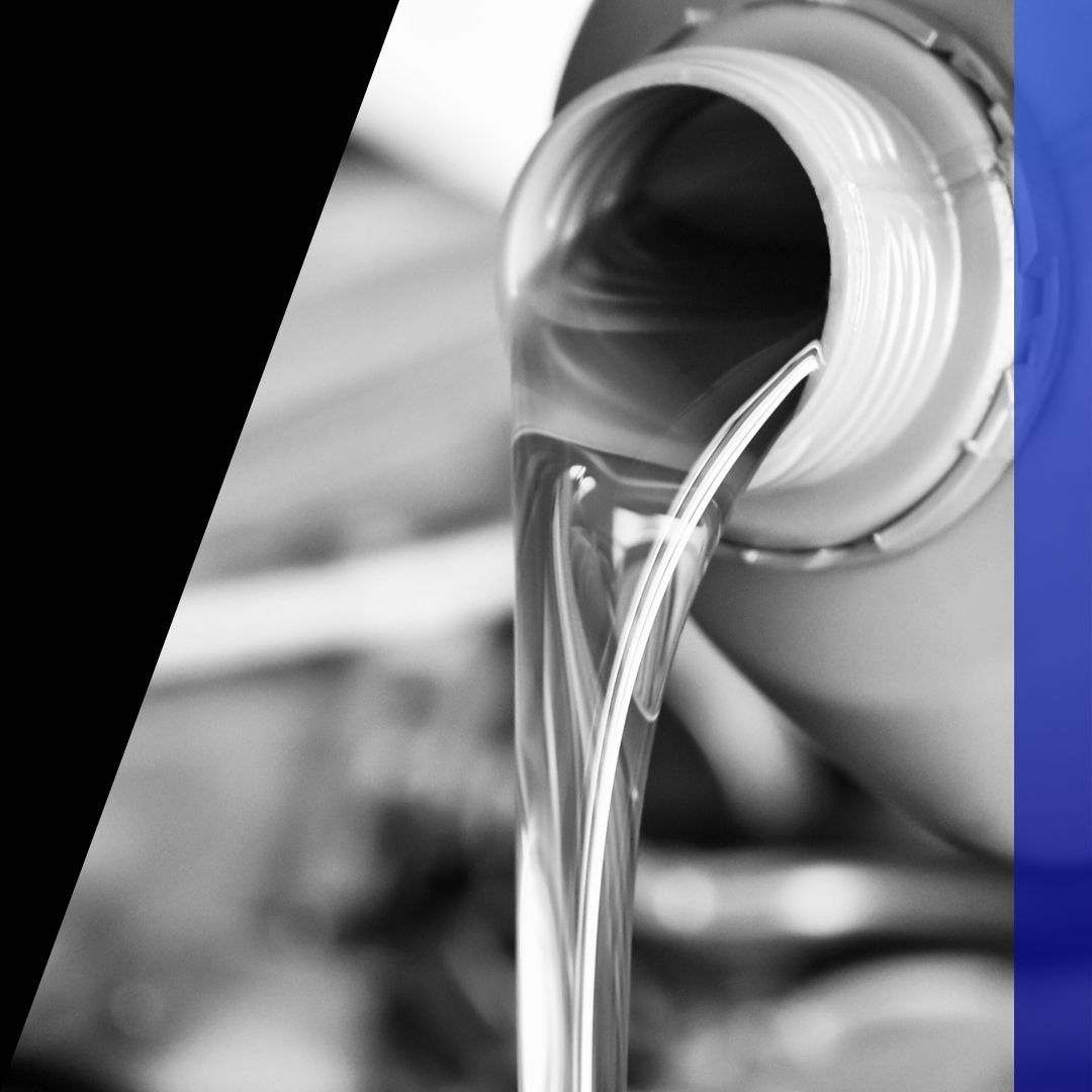 Black and white photo of clean motor oil being poured from a bottle into a car engine, emphasizing quality oil changes.