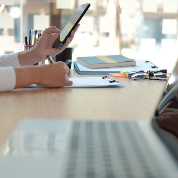 Woman at desk using phone and taking notes