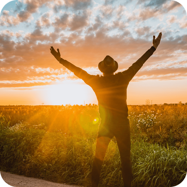 A person stands with arms open wide at a mountain overlook as warm, golden sun rays stream down from the clouds. A person stands with arms open wide at a mountain overlook as warm, golden sun rays stream down from the clouds.