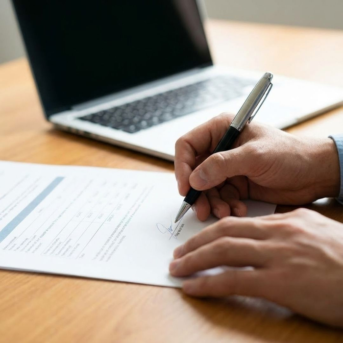 hands signing a financial document on a desk hands signing a financial document on a desk