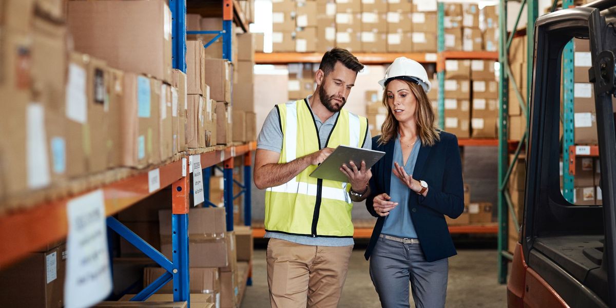 woman in blazer talking to fork lift driver in warehouse