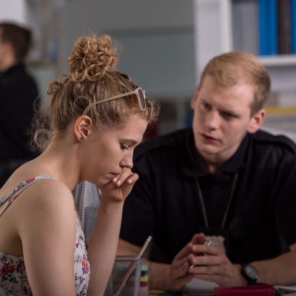 A concerned woman sits at a desk while a police officer talks to her.