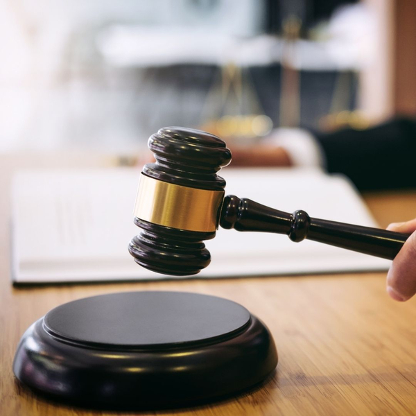 Close-up of a hand holding a judge's gavel, about to strike the sound block.