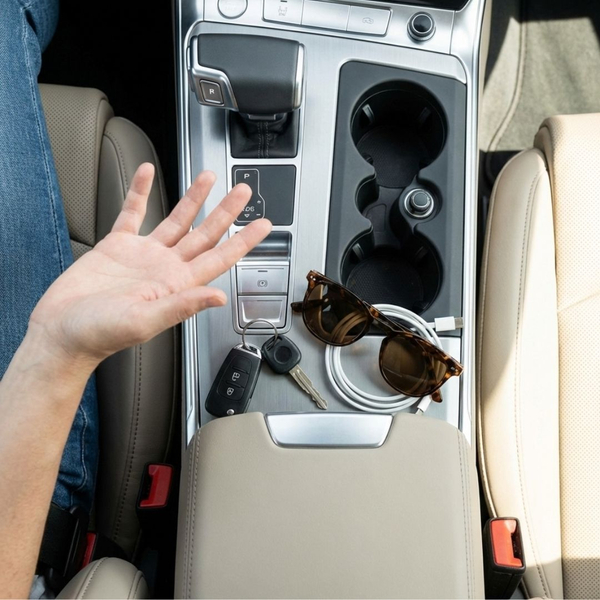 A close-up view of a hand gesturing towards items in a car's center console
