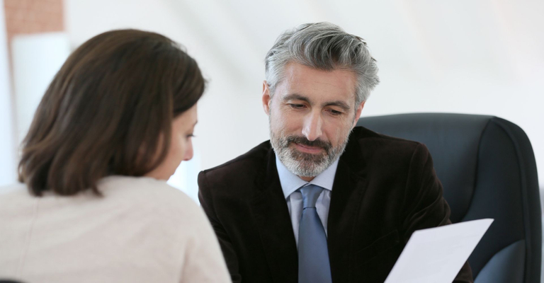 A male lawyer with gray hair reviews a document with a female client. A male lawyer with gray hair reviews a document with a female client.