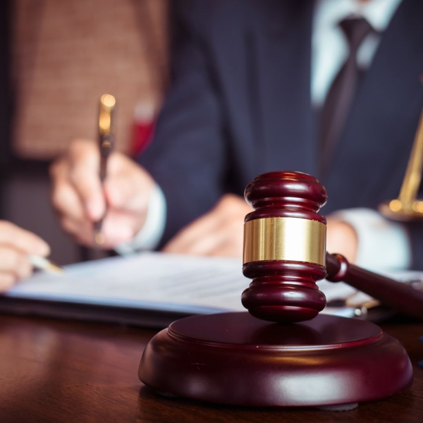 Close-up of a judge's gavel on a desk, with a lawyer signing documents in the background.