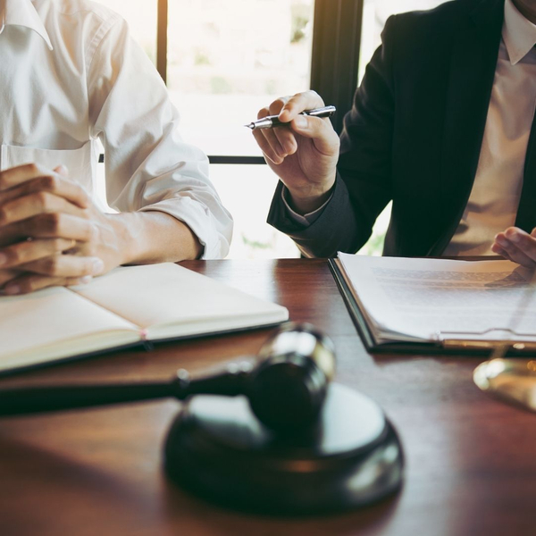A lawyer gestures with a pen while explaining legal documents to a client.