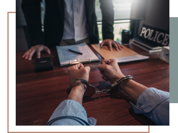 a handcuffed man sitting across a desk from a police officer.